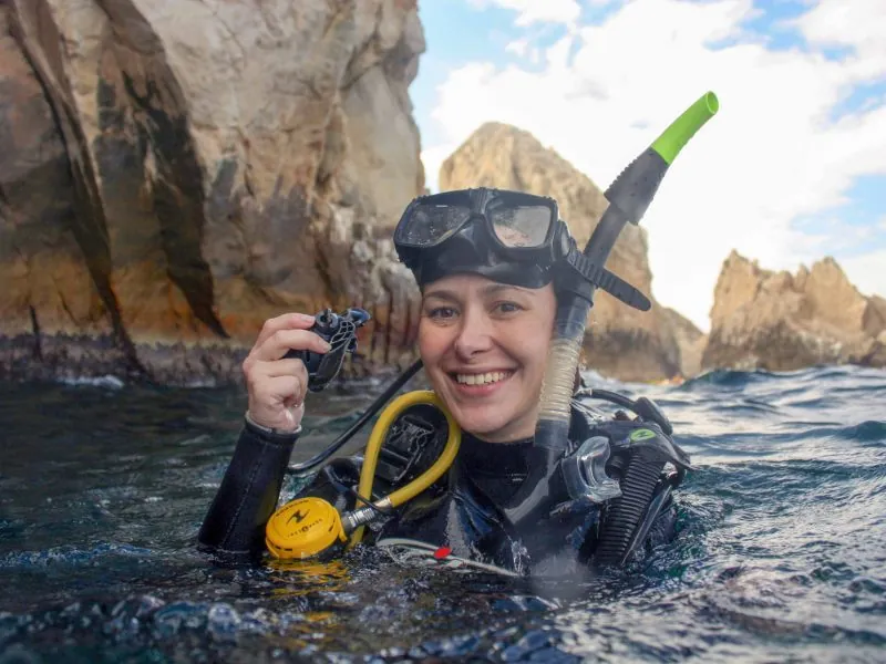 Diver at the surface in mask and wetsuit with the granite islets of Los Arcos behind