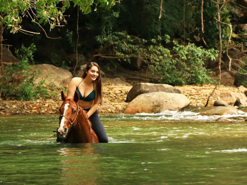 Rider on a horse wading chest-deep in the green water of the Cuale River