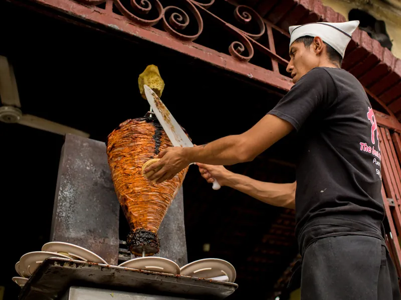 Taquero slicing al pastor from the spit at a Puerto Vallarta taco stand