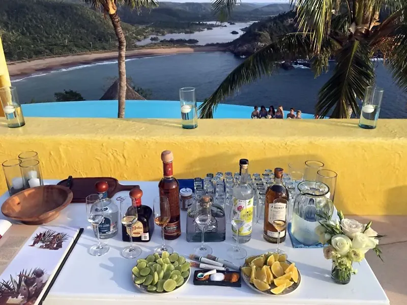 Tasting table with tequila bottles, limes and oranges on a yellow terrace above a Pacific bay
