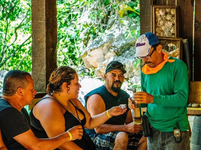 Guide pouring tequila for guests seated under a palapa at the end of the ride