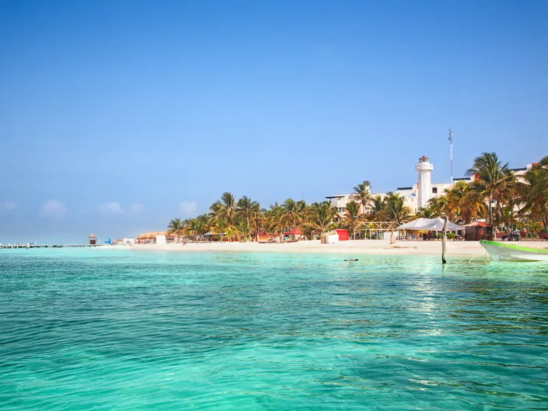 Clear shallow water and a white beach lined with palms and a lighthouse on Isla Mujeres