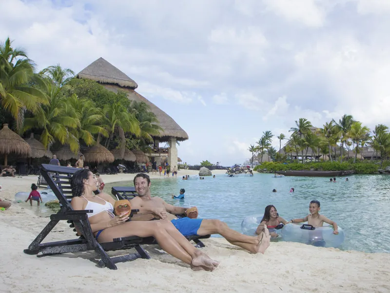 Guests relax on lounge chairs and float in inner tubes at a sandy beach inside Xcaret