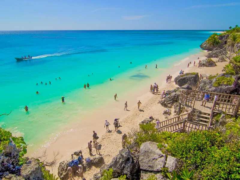 Swimmers and a boat in turquoise water off the beach below the cliffs and wooden stairs at Tulum