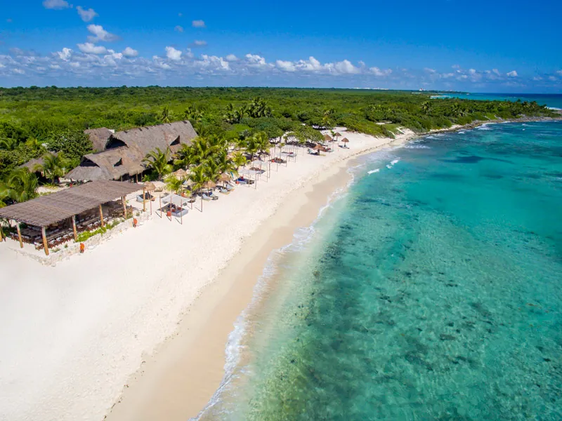 Aerial view of a thatched beach club on white sand beside clear Caribbean water