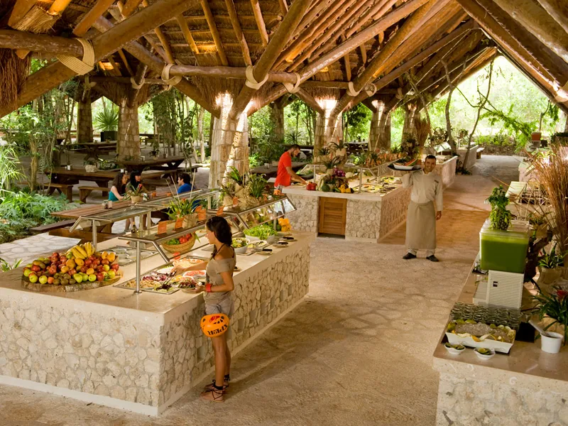A buffet of fruit and dishes under a large open-sided wooden roof at Xplor