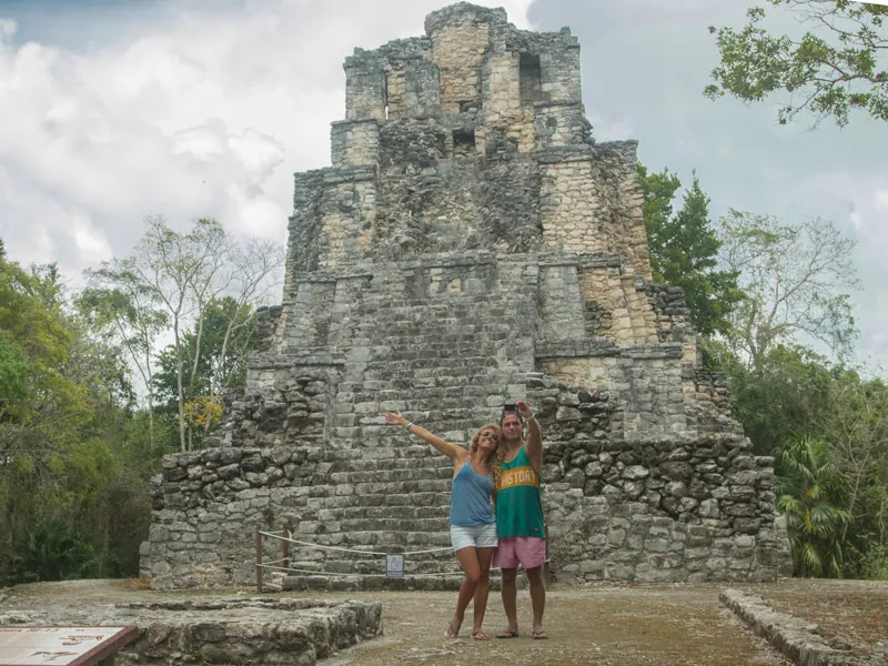 Two visitors in front of the tall stone Castillo pyramid at Muyil, surrounded by jungle