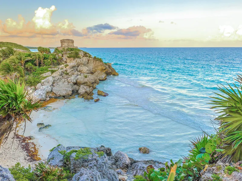 The Tulum castle temple on a rocky headland above a turquoise cove at sunset