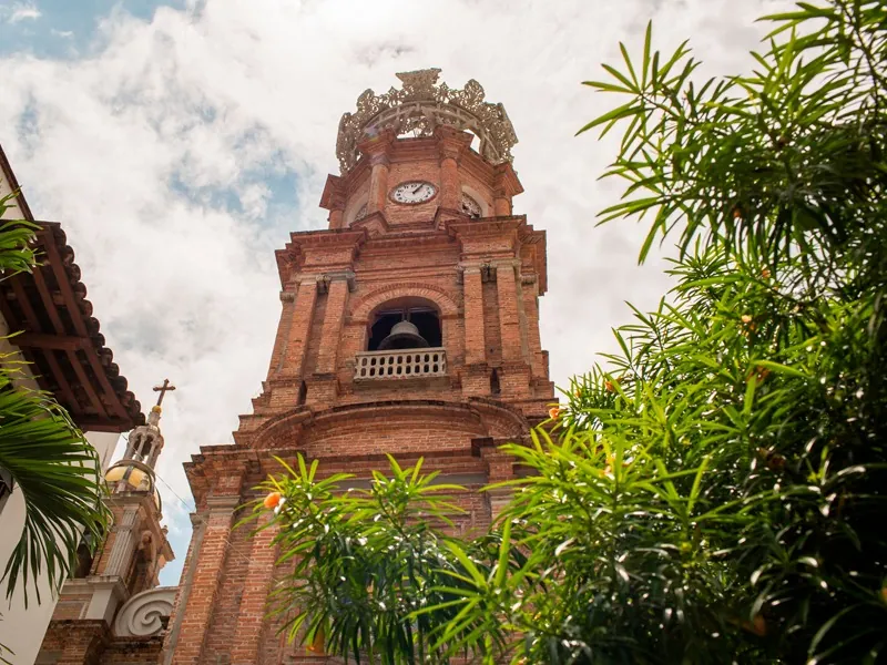 Brick bell tower and crown of the Church of Our Lady of Guadalupe in Puerto Vallarta framed by palms