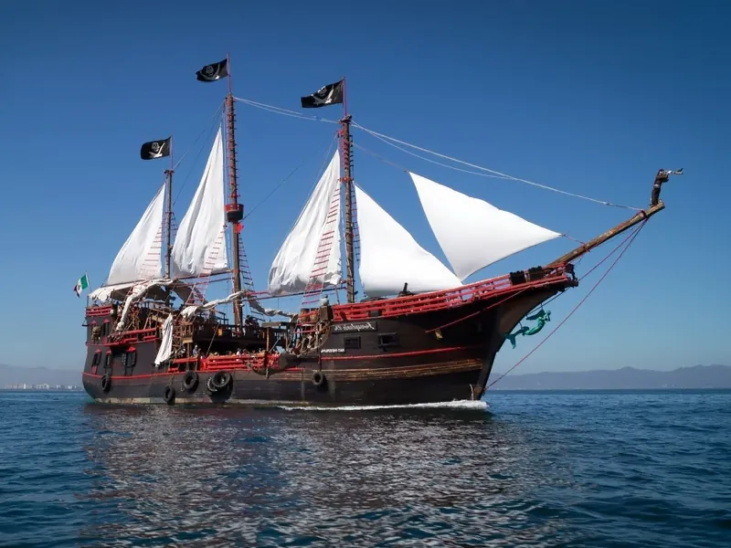 Wooden pirate galleon under full white sail on Banderas Bay, black flags flying