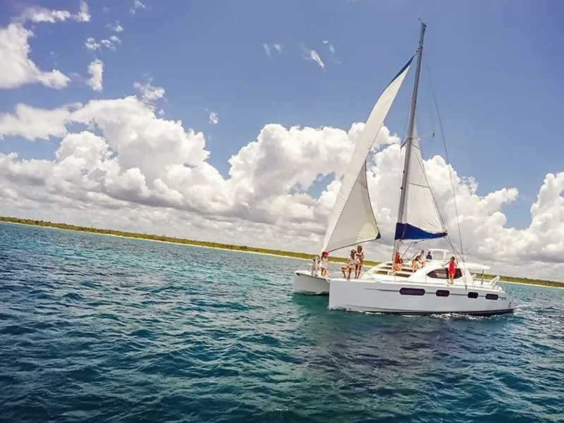 Leopard sailing catamaran under sail with guests on board, clouds over a low coastline