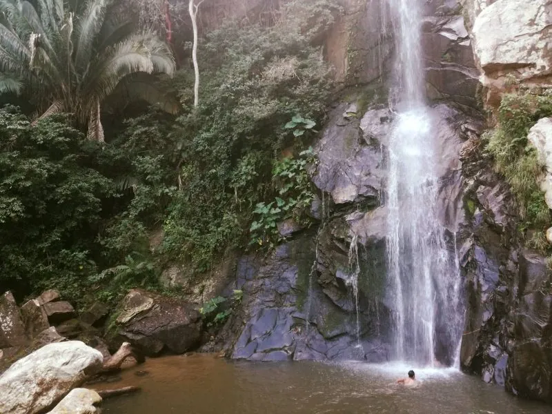 Tall waterfall pouring into a rock pool in the jungle at Quimixto, a swimmer below