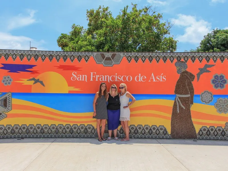 Three guests in front of an orange mural of San Francisco de Asís in San Pancho