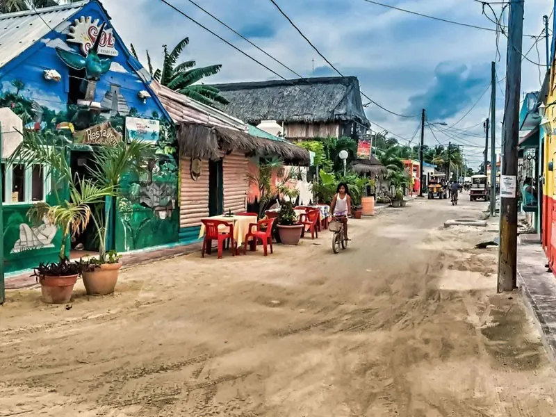 A sandy street in Holbox village with painted buildings, café tables and a cyclist