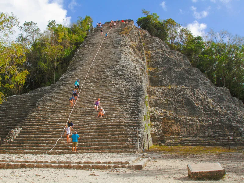 Visitors on the steep stone steps of the main pyramid at Cobá, with forest on either side