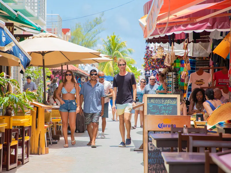 Visitors walking a pedestrian street of shops and café tables in Isla Mujeres town