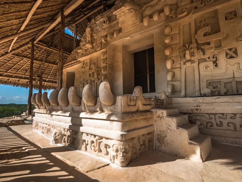 Carved stucco figures and a monster-mouth doorway on the acropolis at Ek Balam, under a thatched roof