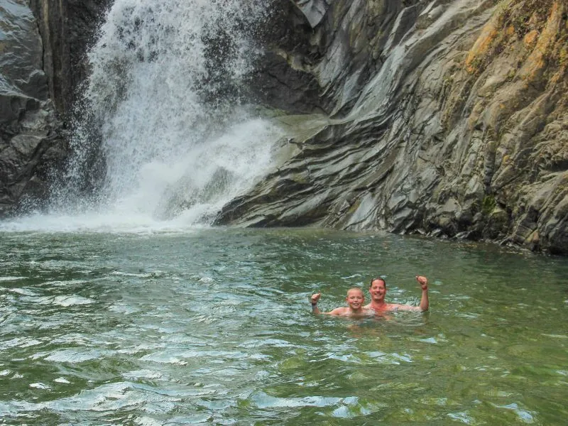 Waterfall pouring over rocks into a swim hole where two guests are swimming