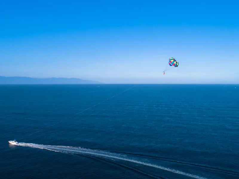 Tow boat leaving a white wake across the bay with a parasail canopy far overhead