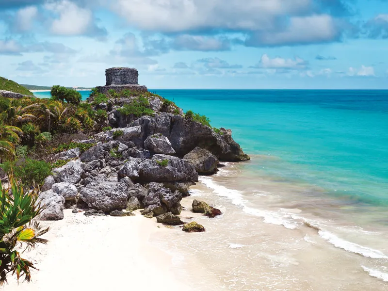 A small stone temple on a rocky headland above a white beach and turquoise water at Tulum