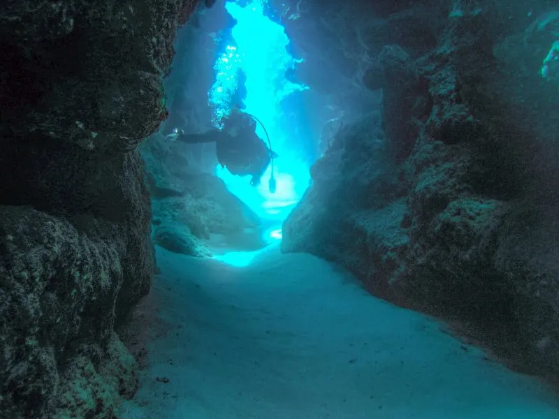 Diver silhouetted in a light-filled rock tunnel underwater at El Morro
