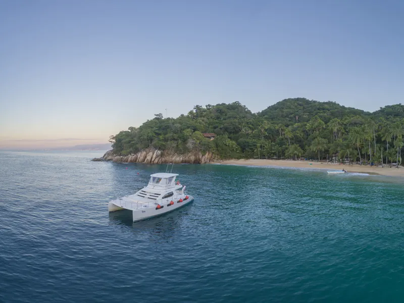 White cruising yacht anchored off a green headland and beach on the South Shore