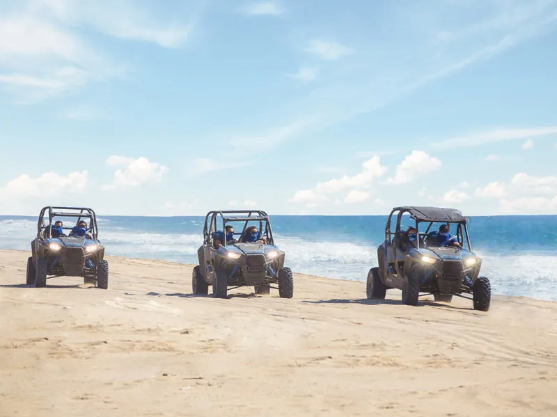 Three UTVs lined up on the sand facing the camera, the sea behind