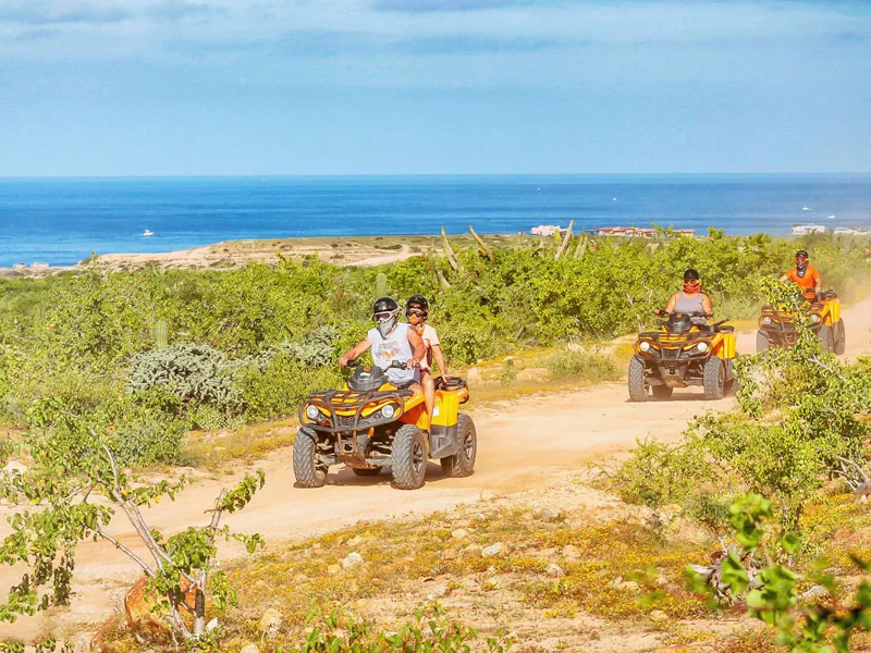 ATVs on a dirt trail through green scrub above the Pacific Ocean in Los Cabos