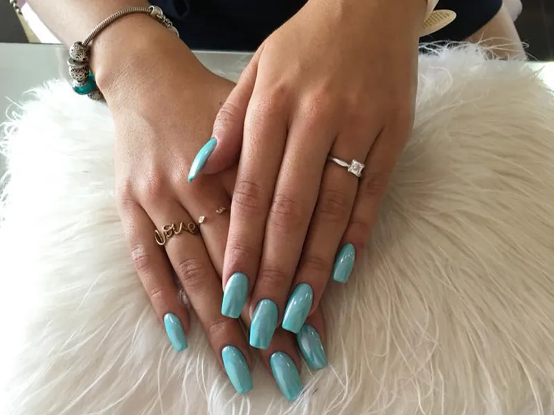 Hands with turquoise gel nails and rings resting on white fur