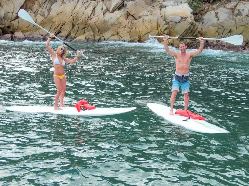 Two guests standing on paddleboards raising their paddles near the islands