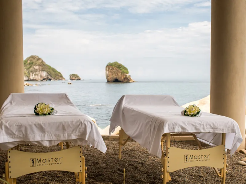Two massage tables set up on a terrace facing the sea and Los Arcos