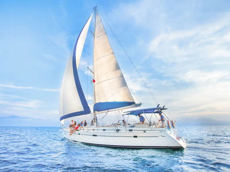 White sailing yacht under full sail with guests on deck under a clear sky