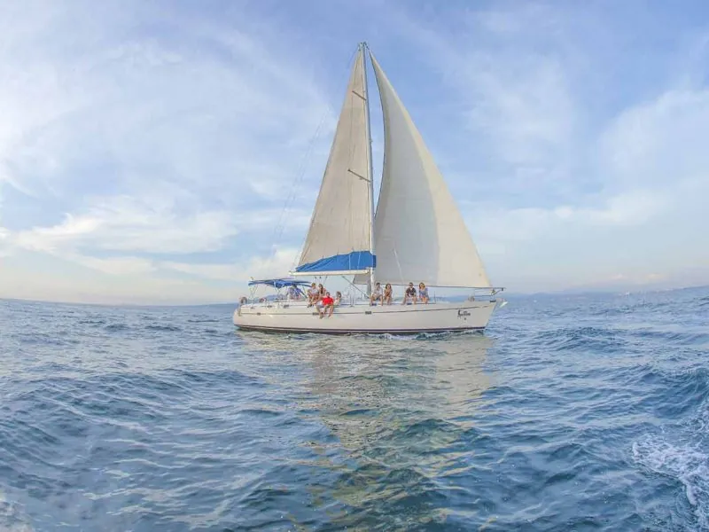White sailboat under full sail with guests on deck, crossing open water on Banderas Bay