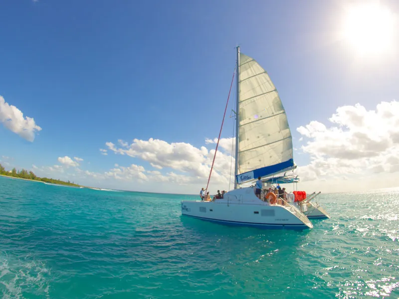 A sailing catamaran with guests on deck on turquoise water under a bright sun