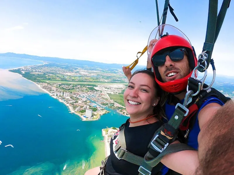Tandem pair under an open parachute above the coastline and marina of Banderas Bay