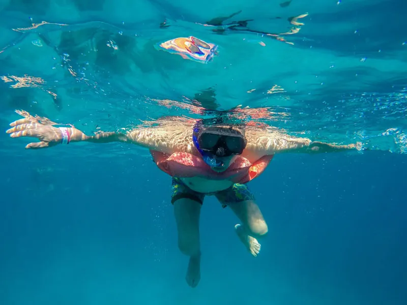 Snorkeler in a life vest seen from below the surface in clear blue water