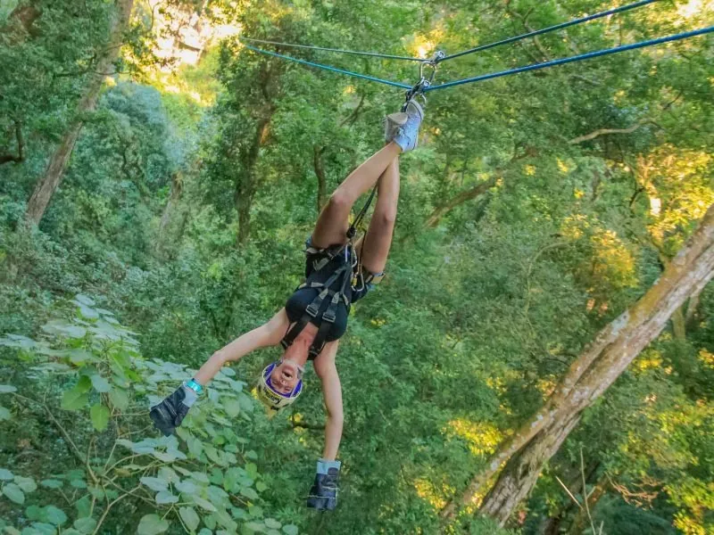 Guest hanging upside down from a zip line trolley among the trees