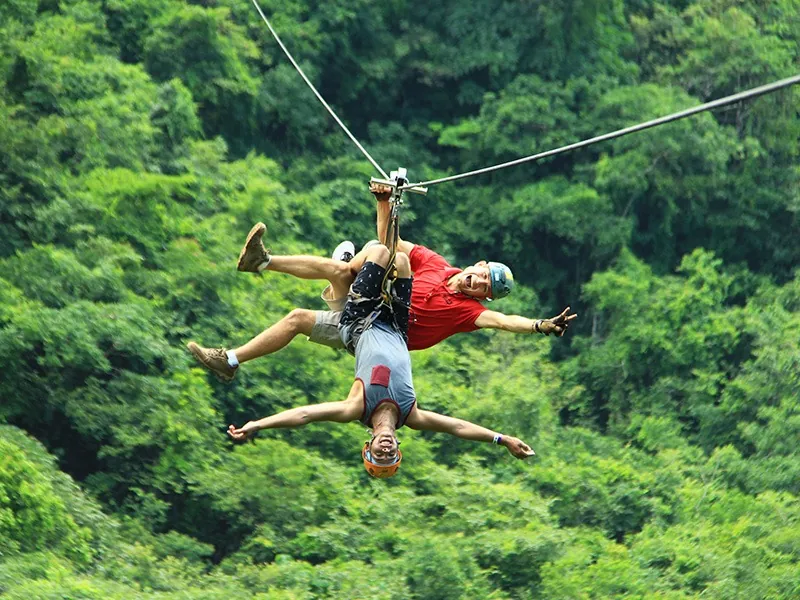 Guest hanging upside down from a zip line above the treetops on the ATV and canopy combo