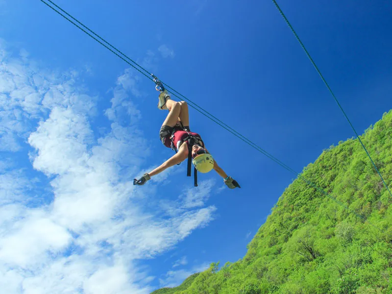 Zip-liner hanging upside down on the cable above a green hillside
