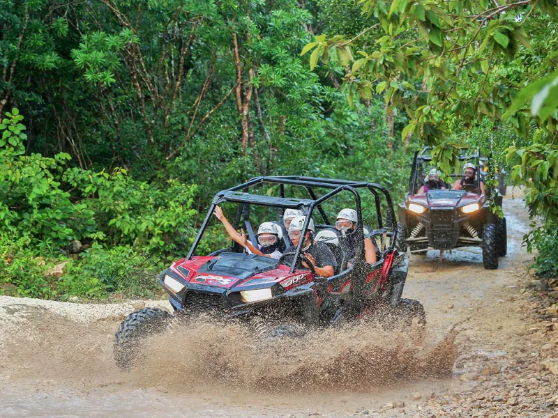 Two Polaris UTVs splashing through a muddy jungle track, drivers and passengers in helmets