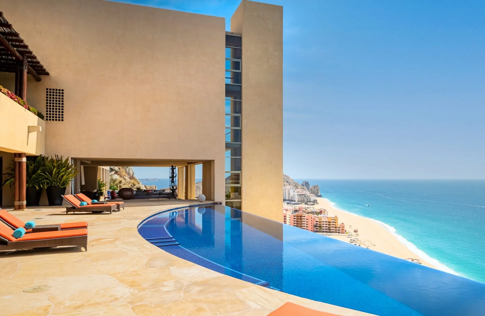 Curved infinity pool on a cliffside terrace looking down on Medano Beach, with the Land's End rock formations on the horizon.
