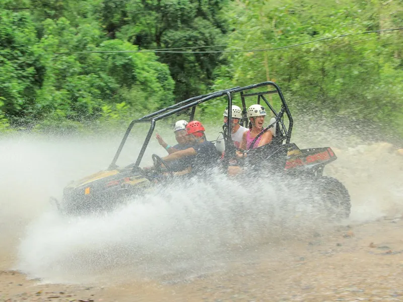 Four-seat all-terrain vehicle throwing a wall of spray as it crosses a river