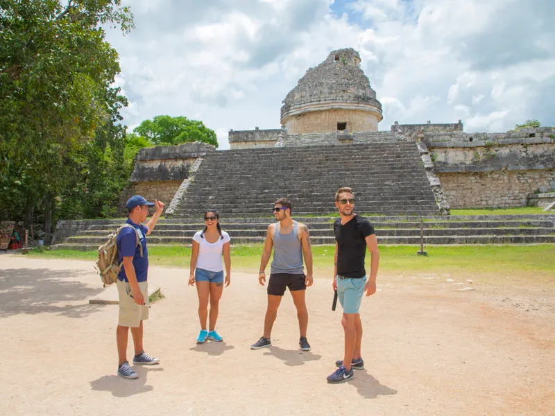 A guide talks with three visitors in front of the observatory at Chichén Itzá