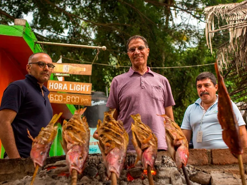 Guests beside whole fish grilling zarandeado-style on sticks over coals