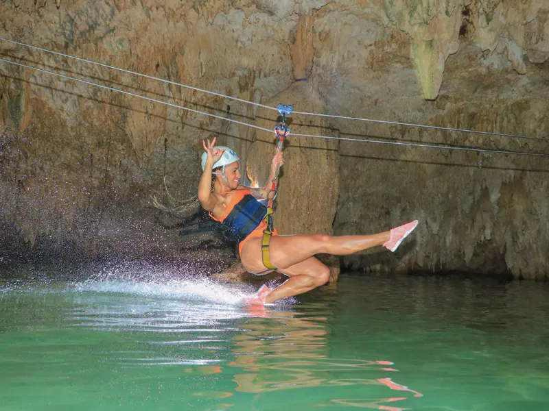 A woman on a zip-line skimming the green water inside a cenote cave
