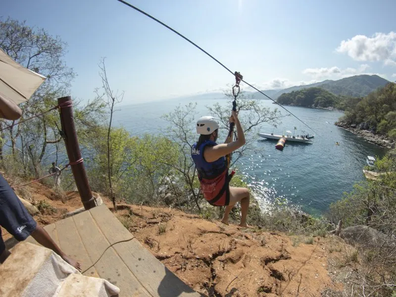Guest in a helmet on a zip-line launching from a rocky point over the sea