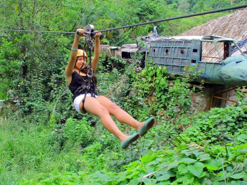 Guest on a zip line passing a wrecked aircraft prop and palapa in the jungle at El Edén